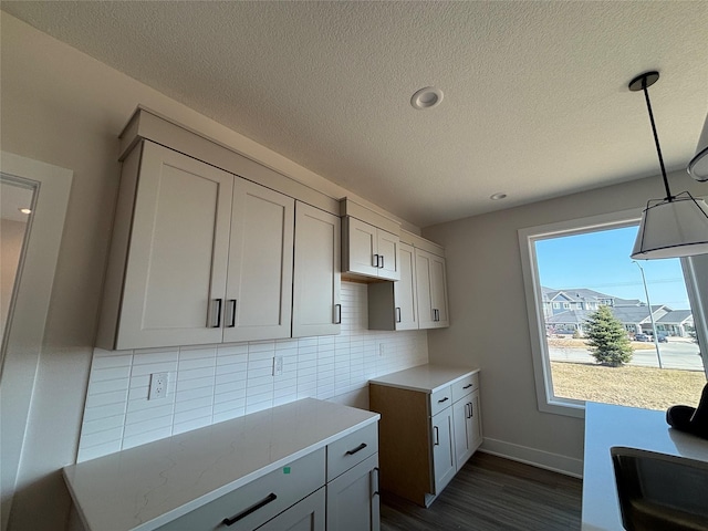 kitchen with dark wood-type flooring, a textured ceiling, decorative backsplash, baseboards, and hanging light fixtures