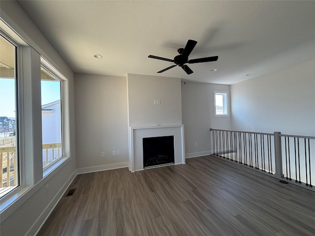 unfurnished living room featuring visible vents, baseboards, a fireplace, dark wood-style floors, and a textured ceiling