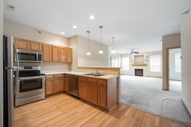 kitchen featuring appliances with stainless steel finishes, pendant lighting, sink, kitchen peninsula, and light wood-type flooring