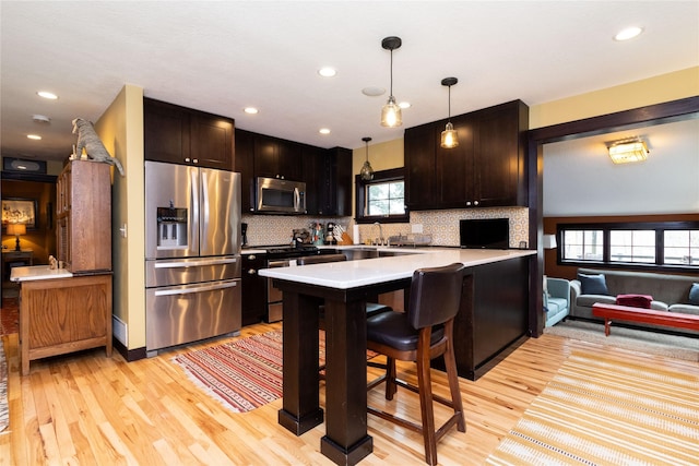 kitchen with a breakfast bar, appliances with stainless steel finishes, tasteful backsplash, decorative light fixtures, and kitchen peninsula