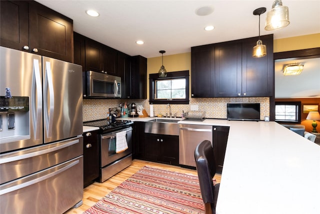 kitchen featuring sink, decorative light fixtures, light hardwood / wood-style flooring, stainless steel appliances, and backsplash