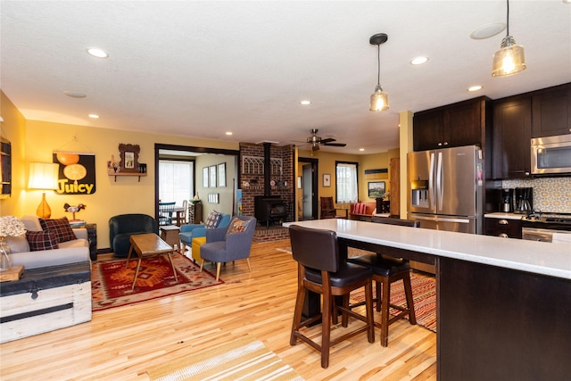 kitchen featuring pendant lighting, appliances with stainless steel finishes, backsplash, dark brown cabinets, and light wood-type flooring