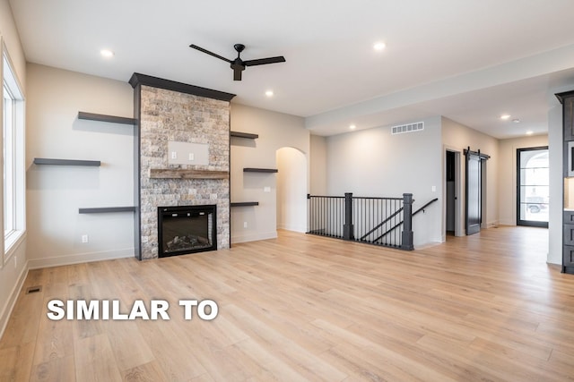 unfurnished living room featuring a fireplace, light hardwood / wood-style flooring, a barn door, and ceiling fan