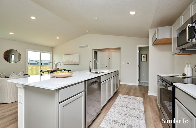 kitchen with sink, light hardwood / wood-style flooring, appliances with stainless steel finishes, a center island with sink, and vaulted ceiling