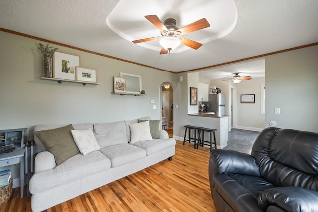 living room featuring wood-type flooring, ornamental molding, ceiling fan, and a textured ceiling