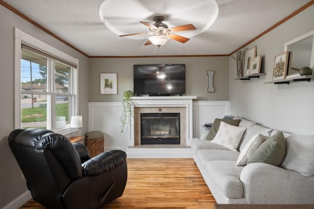 living room with crown molding, wood-type flooring, a tiled fireplace, and a textured ceiling