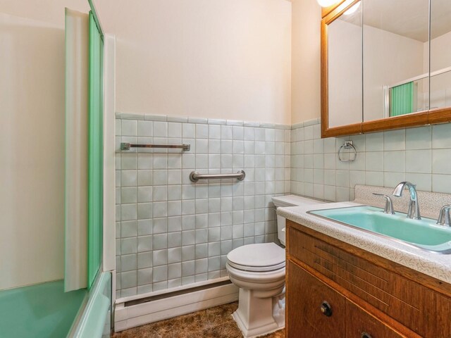 full bathroom featuring bath / shower combo with glass door, tile walls, vanity, a baseboard heating unit, and toilet