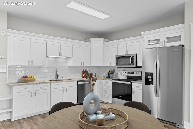 kitchen with sink, appliances with stainless steel finishes, white cabinetry, backsplash, and light stone countertops