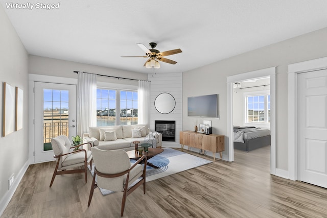 living room with ceiling fan, a large fireplace, and light hardwood / wood-style floors