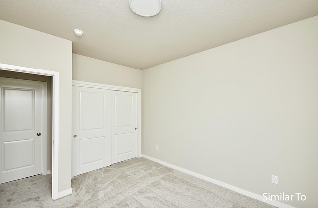 unfurnished bedroom with a closet, light carpet, and a textured ceiling