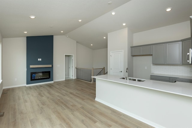 6433 NE 11th Ct, Des Moines, IA 50313 - kitchen with gray cabinetry, a sink, tasteful backsplash, light wood-style floors, and lofted ceiling