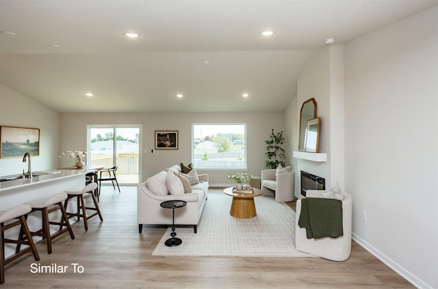 living area featuring a glass covered fireplace, vaulted ceiling, recessed lighting, and light wood-style floors