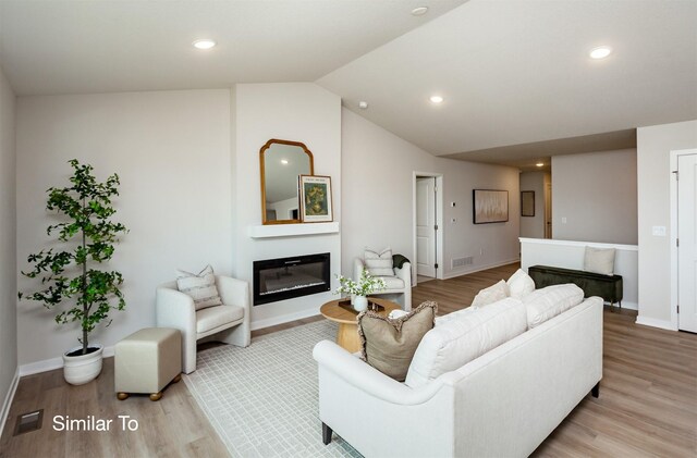 living room featuring visible vents, wood finished floors, a glass covered fireplace, baseboards, and vaulted ceiling