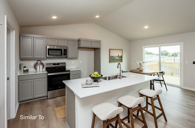 kitchen featuring light wood-type flooring, gray cabinets, a sink, stainless steel appliances, and vaulted ceiling