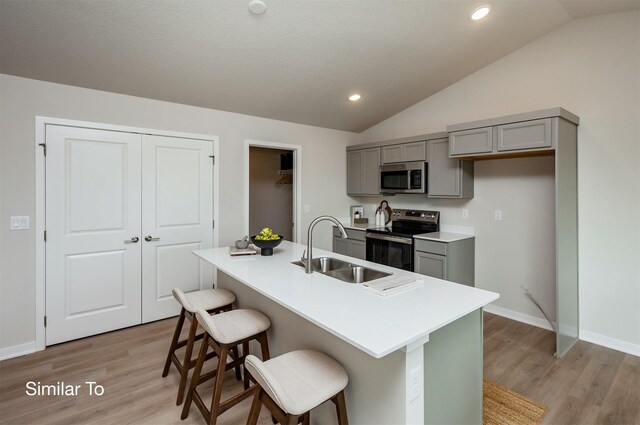 kitchen featuring gray cabinets, a sink, vaulted ceiling, appliances with stainless steel finishes, and a kitchen bar