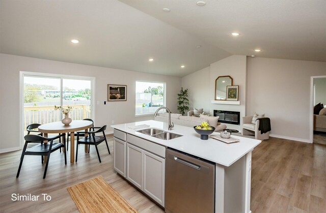 kitchen featuring open floor plan, light countertops, stainless steel dishwasher, a glass covered fireplace, and a sink