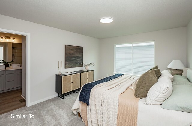 bedroom featuring light carpet, ensuite bath, baseboards, and a sink