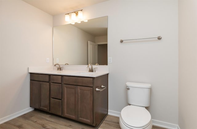 bathroom featuring double vanity, wood finished floors, toilet, and a sink