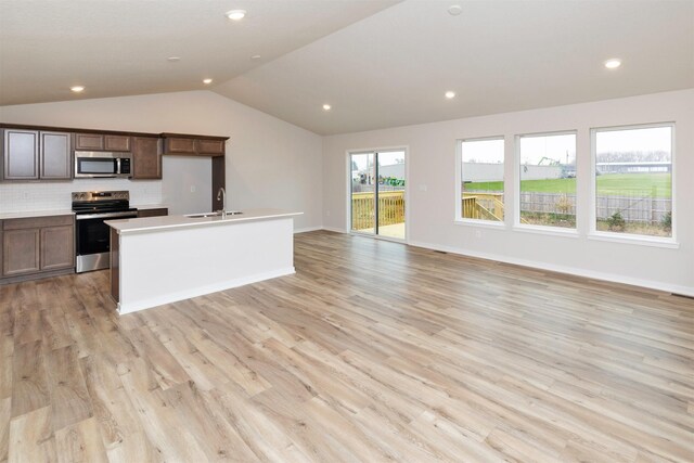 kitchen featuring a sink, light wood-type flooring, backsplash, lofted ceiling, and appliances with stainless steel finishes
