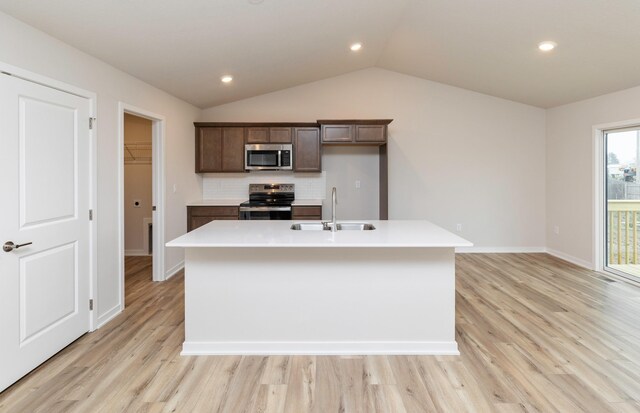 kitchen with a sink, light wood-type flooring, stainless steel appliances, a center island with sink, and light countertops