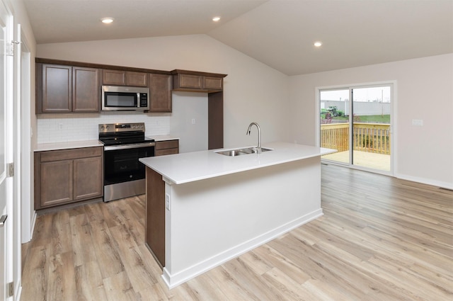 kitchen with stainless steel appliances, light wood-style flooring, a sink, backsplash, and lofted ceiling