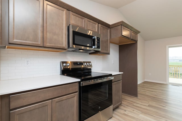 kitchen with backsplash, lofted ceiling, light wood-style flooring, and stainless steel appliances