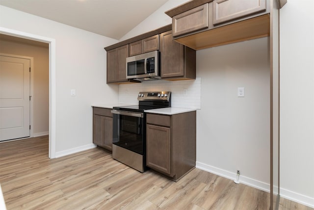 kitchen with vaulted ceiling, tasteful backsplash, stainless steel appliances, and light wood finished floors
