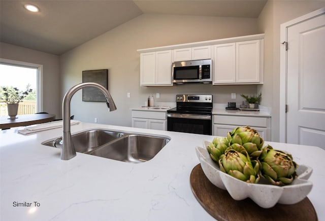 kitchen with vaulted ceiling, appliances with stainless steel finishes, sink, white cabinets, and light stone countertops