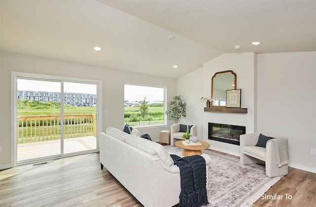 living room with light hardwood / wood-style flooring, vaulted ceiling, and a textured ceiling