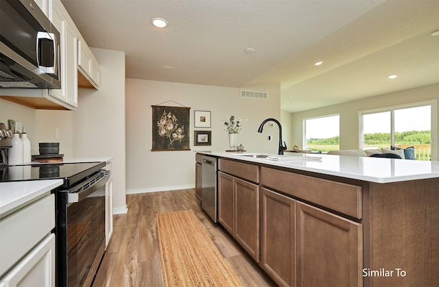 kitchen with sink, white cabinetry, light hardwood / wood-style floors, stainless steel appliances, and a kitchen island with sink