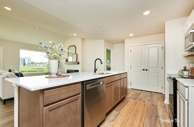 kitchen with sink, light hardwood / wood-style flooring, dishwasher, a kitchen island with sink, and black / electric stove