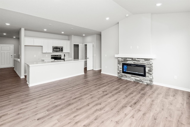 6423 NE 11th Ct, Des Moines, IA 50313 - unfurnished living room featuring light wood-style flooring, recessed lighting, a stone fireplace, baseboards, and vaulted ceiling