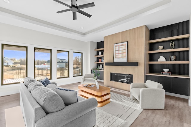 living room featuring a raised ceiling, ceiling fan, light hardwood / wood-style floors, and built in shelves