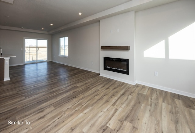 unfurnished living room with light wood-type flooring, a glass covered fireplace, baseboards, and recessed lighting