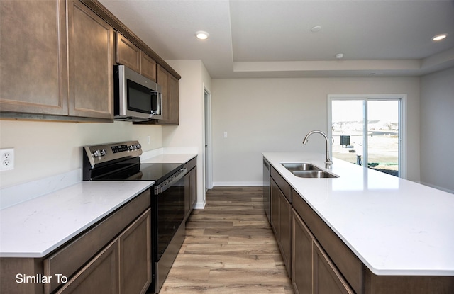 kitchen featuring stainless steel appliances, sink, a kitchen island with sink, and light hardwood / wood-style flooring