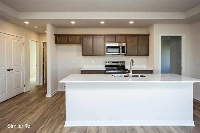 kitchen featuring a kitchen island with sink, sink, wood-type flooring, and appliances with stainless steel finishes