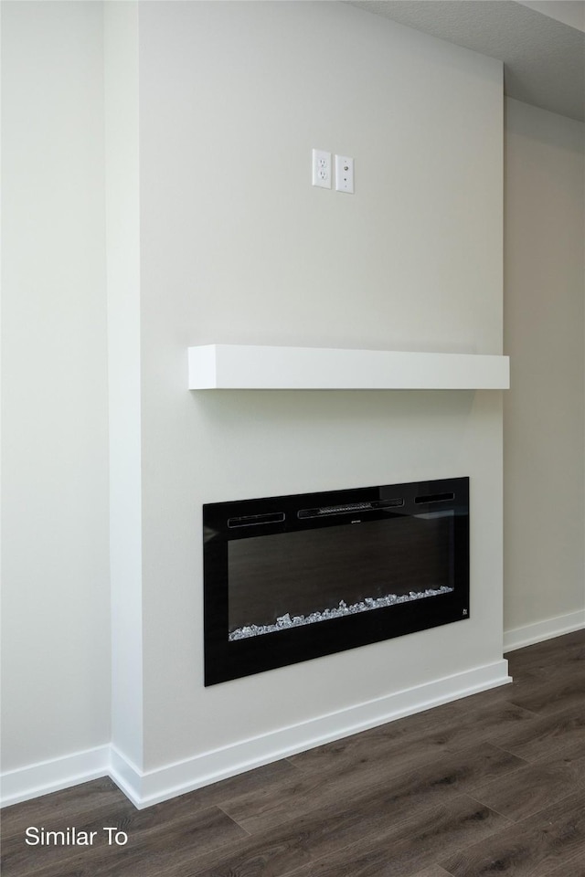 interior details with wood finished floors, a glass covered fireplace, and baseboards