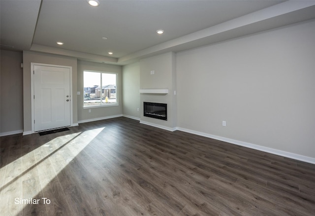 unfurnished living room with baseboards, dark wood-style flooring, a tray ceiling, and recessed lighting