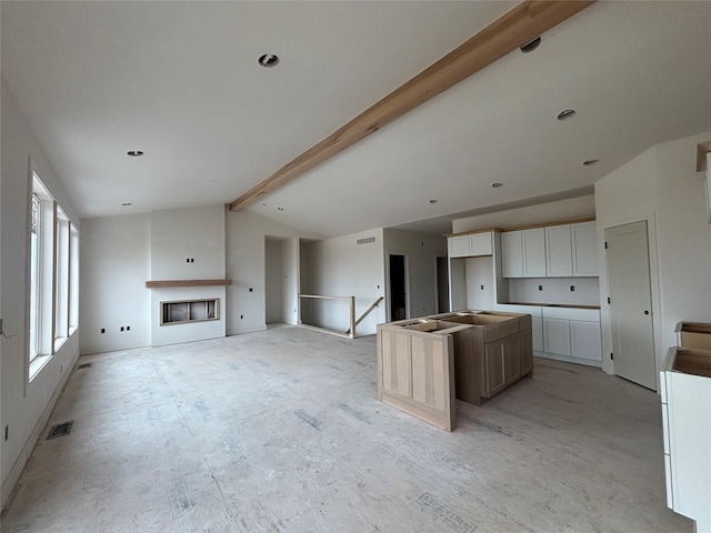 kitchen with visible vents, a kitchen island, lofted ceiling with beams, a fireplace, and white cabinets