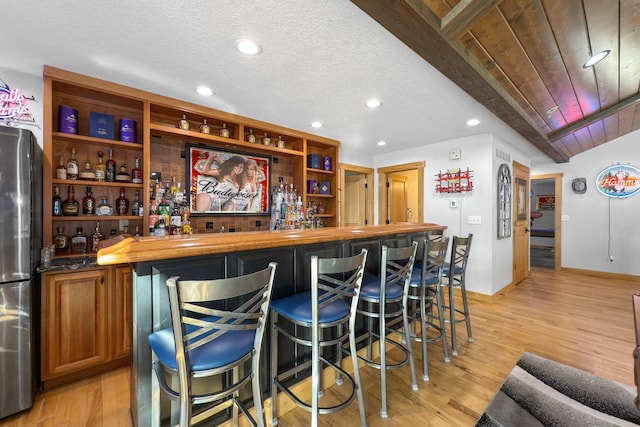 bar with stainless steel refrigerator, wooden counters, a textured ceiling, and light wood-type flooring