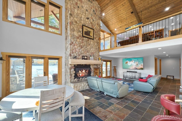 living room with a towering ceiling, a stone fireplace, and wooden ceiling