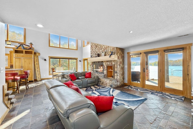 living room with a water view, a stone fireplace, a textured ceiling, and a wealth of natural light