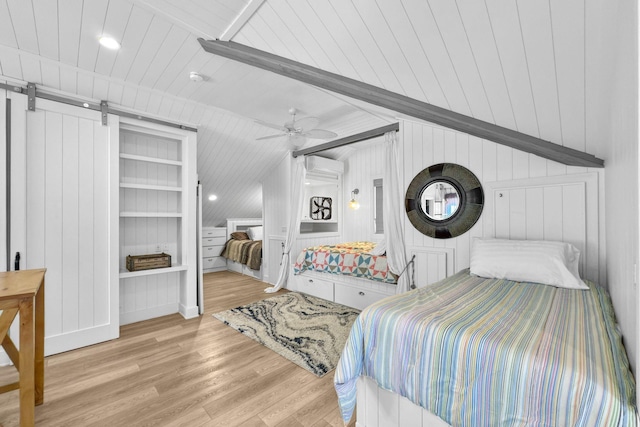 bedroom featuring vaulted ceiling, an AC wall unit, ceiling fan, a barn door, and light hardwood / wood-style flooring