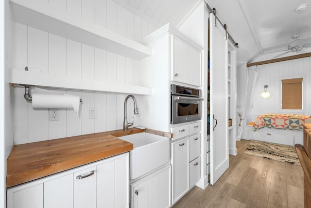 kitchen featuring white cabinetry, sink, oven, a barn door, and light hardwood / wood-style flooring