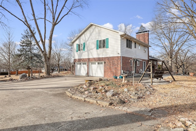 view of home's exterior with concrete driveway, brick siding, a chimney, and an attached garage