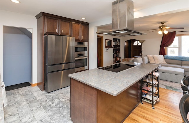 kitchen with ceiling fan, appliances with stainless steel finishes, light stone counters, dark brown cabinetry, and island range hood