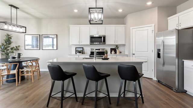 kitchen with white cabinetry, stainless steel appliances, an island with sink, and hanging light fixtures