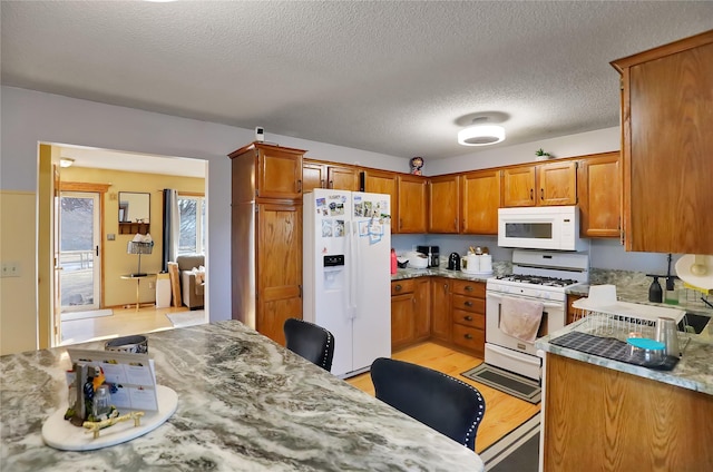 kitchen with light stone counters, a textured ceiling, white appliances, and light hardwood / wood-style floors