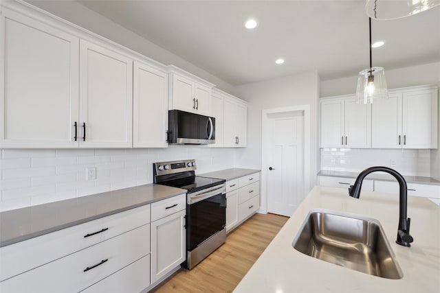 kitchen featuring a sink, decorative light fixtures, appliances with stainless steel finishes, white cabinets, and light wood finished floors