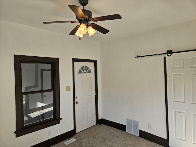 foyer entrance featuring a barn door, carpet, and ceiling fan